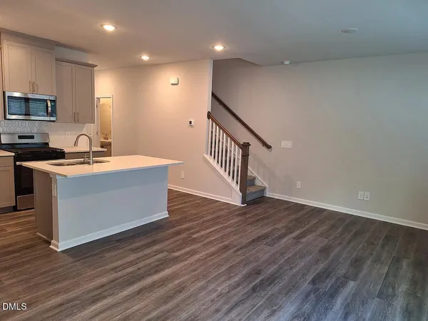 a view of a kitchen with kitchen island a sink wooden floor and black appliances