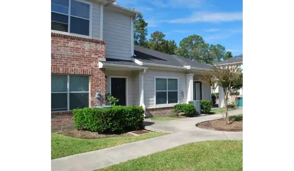 a view of a house with brick walls plants and large tree