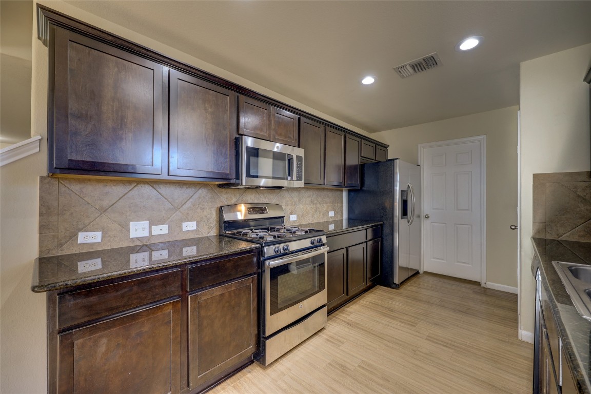 267 Voyager Cove Kyle, TX 78640 - Photo 13 of 40 a kitchen with stainless steel appliances granite countertop a stove top oven a sink and dishwasher a refrigerator with wooden floor