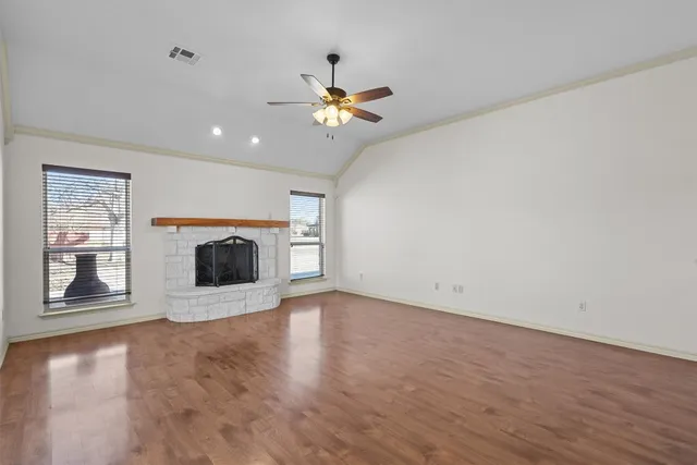 an empty room with windows fireplace and a kitchen view