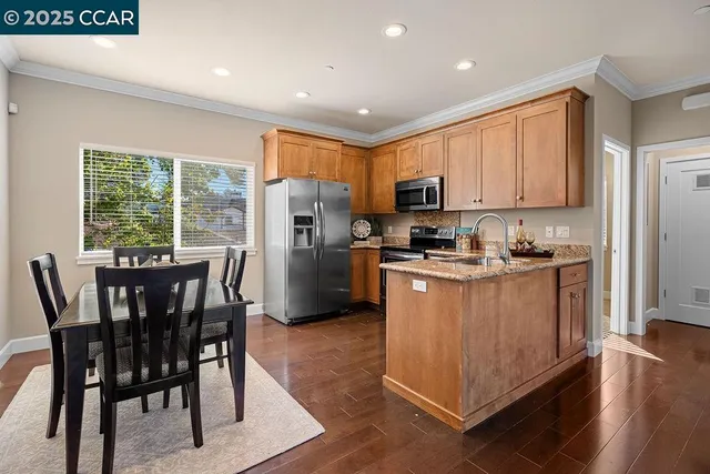 a kitchen with stainless steel appliances granite countertop a stove a refrigerator a microwave oven with a dining table and chairs with wooden floor
