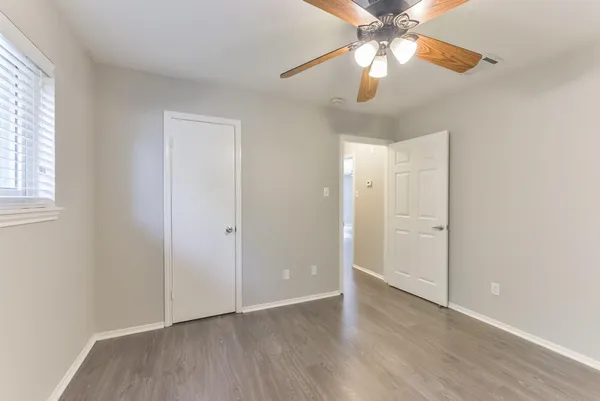 an empty room with wooden floor fan and windows