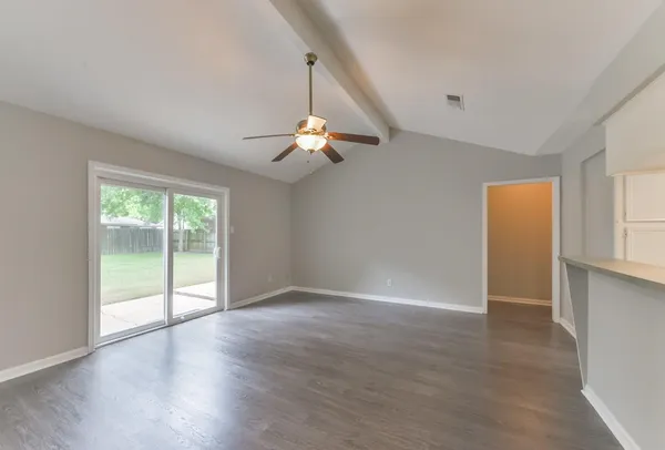 an empty room with wooden floor fan and windows