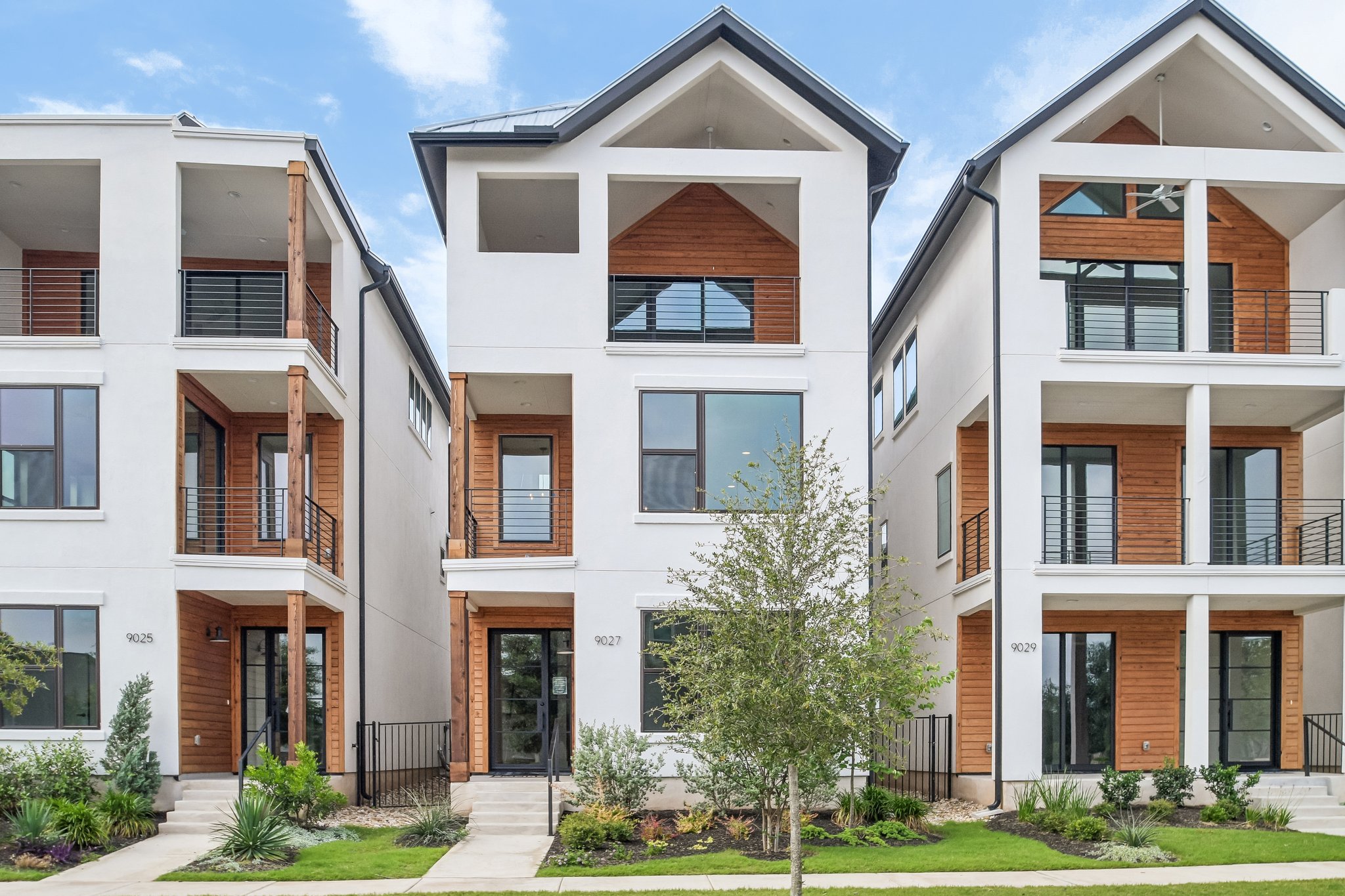 These modern residences combine crisp white stucco with warm wood accents, creating a striking facade with multiple private balconies.