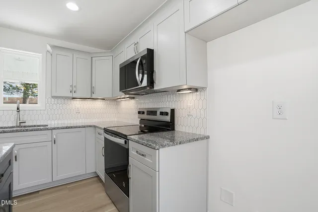 a kitchen with stainless steel appliances granite countertop white cabinets a microwave a sink and a counter