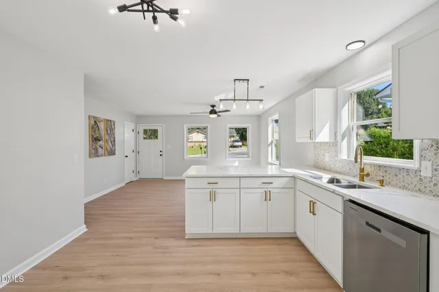 a view of a kitchen with a sink dishwasher a stove and white cabinets with wooden floor