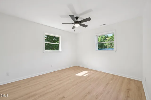 an empty room with wooden floor ceiling fan and windows