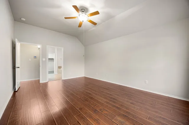 a view of an empty room with wooden floor and a ceiling fan