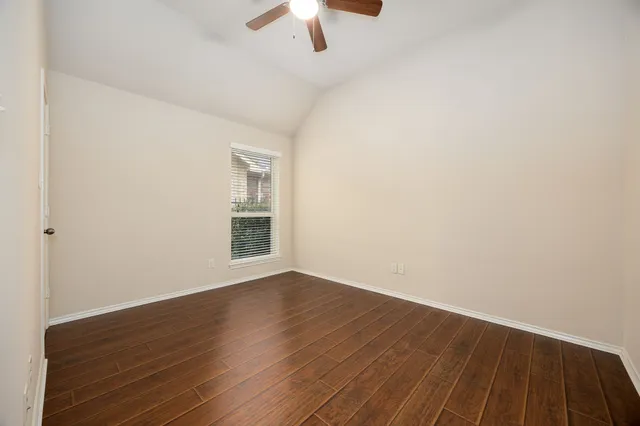 a view of an empty room with wooden floor ceiling fan