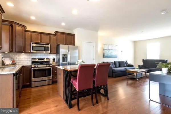 a kitchen with stainless steel appliances granite countertop a stove top oven a sink dishwasher a dining table and chairs with wooden floor