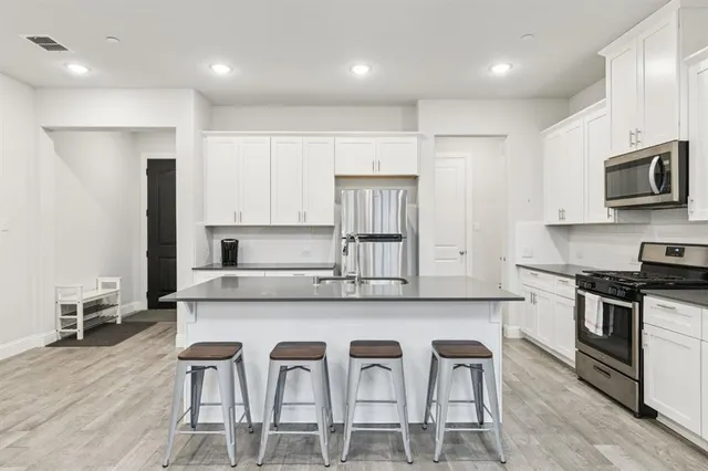 a kitchen with stainless steel appliances a stove a sink a microwave a refrigerator and white cabinets