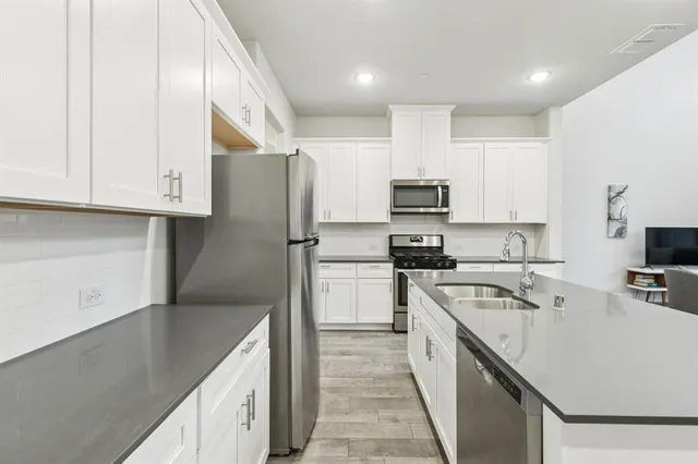 a kitchen with stainless steel appliances granite countertop a stove top oven a sink a refrigerator and white cabinets with wooden floor