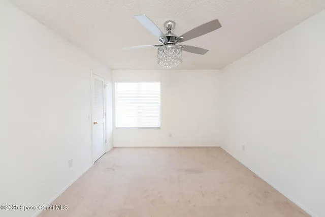 an empty room with a chandelier fan and windows