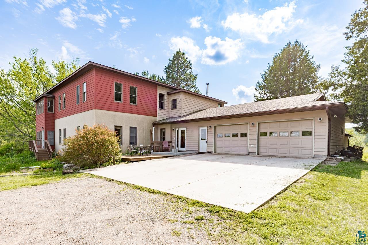 4800 Tower Road Moose Lake, MN 55767 - Photo 40 of 83 Exterior featuring red siding and stucco finishes, a multi-level deck, a concrete patio, and a two-car garage with panel doors and upper window inserts