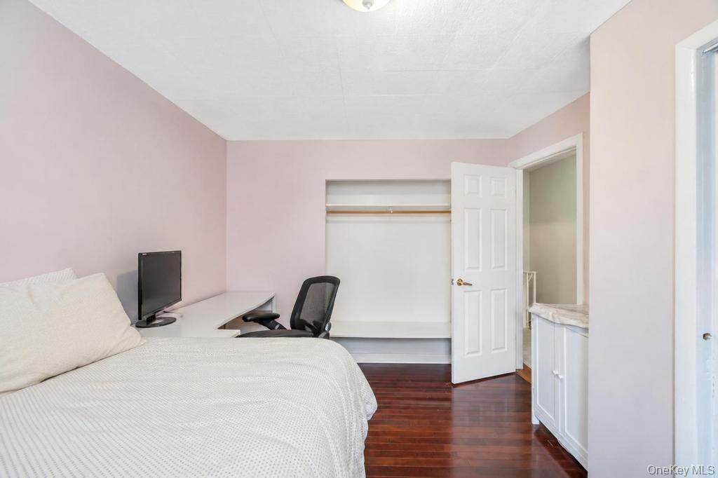 89-13 84th Street Queens, NY 11421 - Photo 26 of 34 Bedroom featuring rich wood-finish flooring, light-toned walls, an open closet with a hanging rod, and a built-in cabinet with a stone-finish countertop