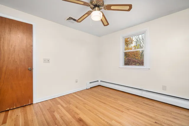 a view of empty room with wooden floor and fan