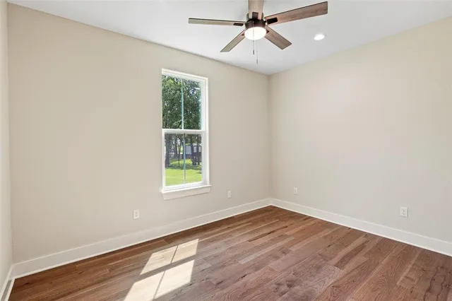 an empty room with wooden floor fan and windows