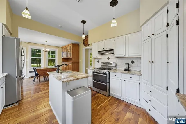 a kitchen with stainless steel appliances kitchen island granite countertop a stove a sink a refrigerator and white cabinets with wooden floor