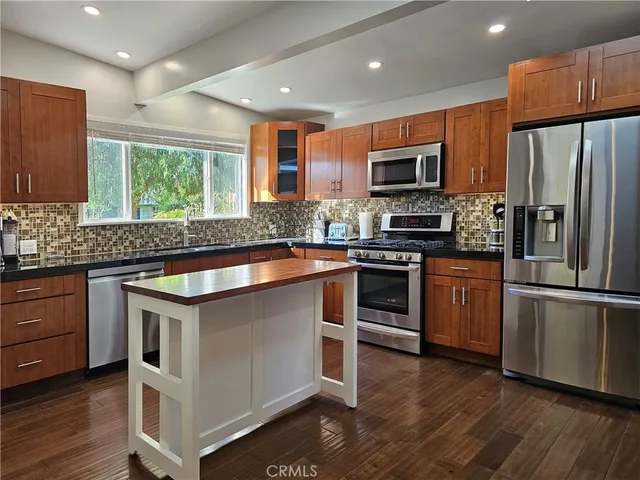 a kitchen with stainless steel appliances granite countertop a stove a sink dishwasher a refrigerator and a microwave oven with wooden floor