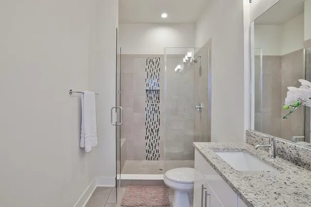 a bathroom with a granite countertop sink a toilet a mirror and shower