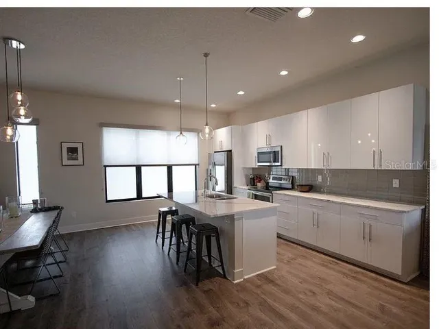 a open kitchen with stainless steel appliances granite countertop a stove a sink dishwasher a dining table and chairs with wooden floor