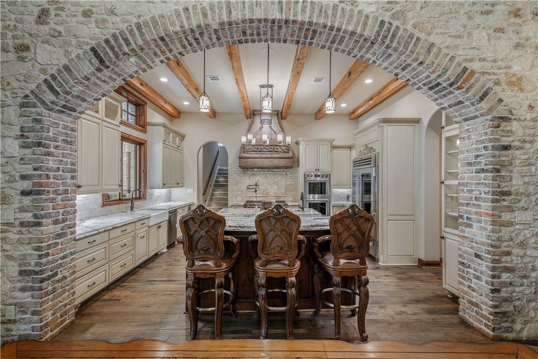 4207 Tuscany Court Bryan, TX 77802 - Photo 20 of 50 Kitchen featuring arched walkways, light stone counters, tasteful backsplash, a kitchen island, and beam ceiling