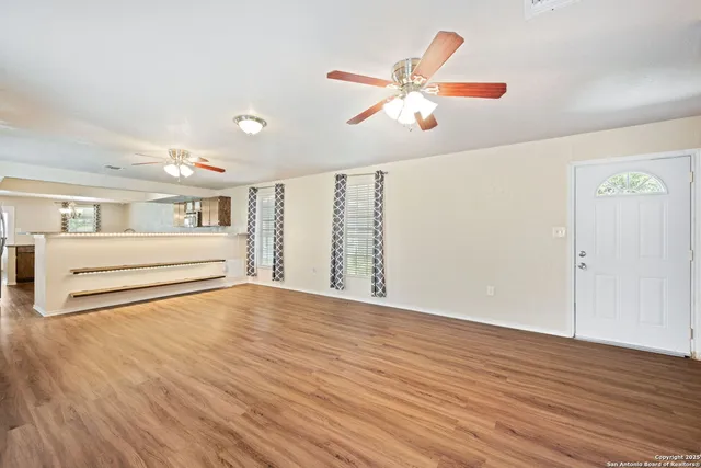a view of an empty room with wooden floor and a ceiling fan