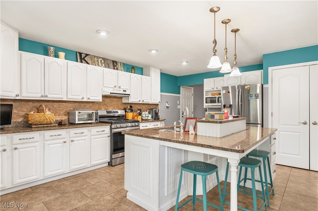 155 Ridgewood Boulevard Belpre, OH 45714 - Photo 19 of 49 Kitchen with decorative backsplash, stainless steel appliances, a kitchen bar, white cabinets, and decorative light fixtures
