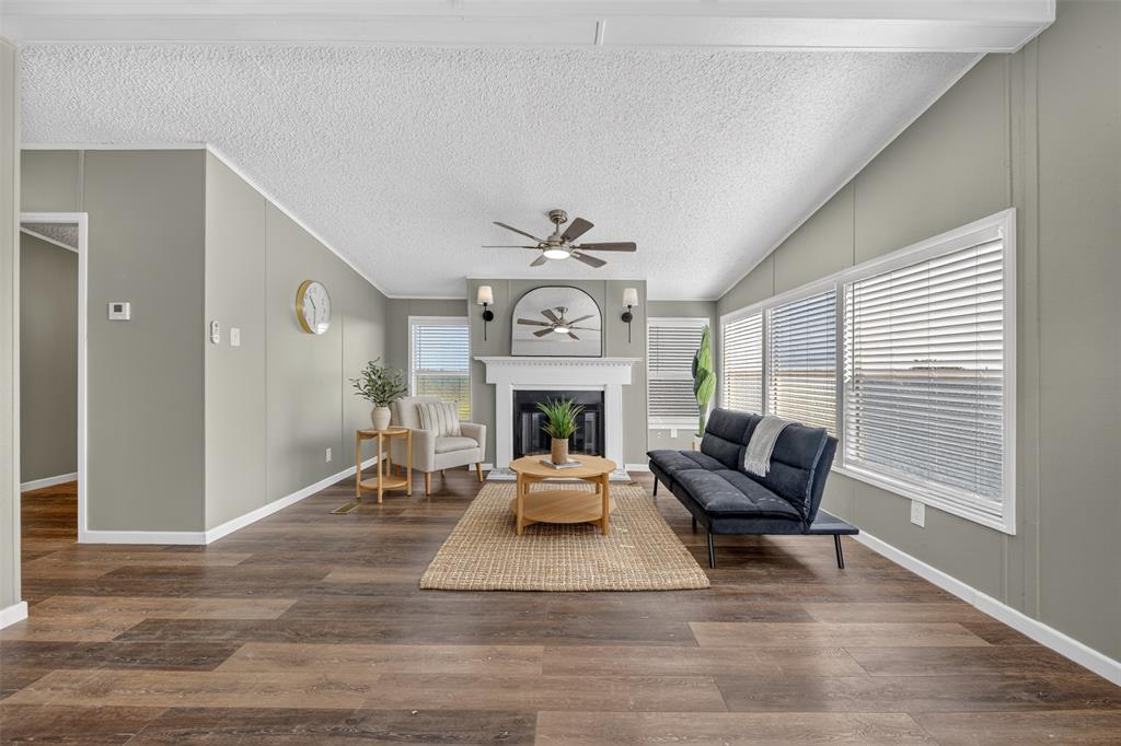 449 Big Salty Lane Springtown, TX 76082 - Photo 11 of 25 Open-concept living space featuring wood-finish flooring, a vaulted ceiling, and a prominent fireplace with a white mantel