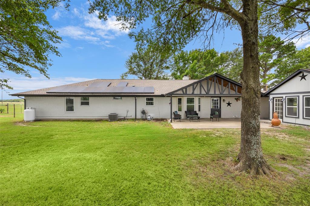 6754 Raymond Road Kaufman, TX 75142 - Photo 29 of 38 Spacious rear yard with a paved patio, white exterior siding, and a gabled roofline featuring solar panels