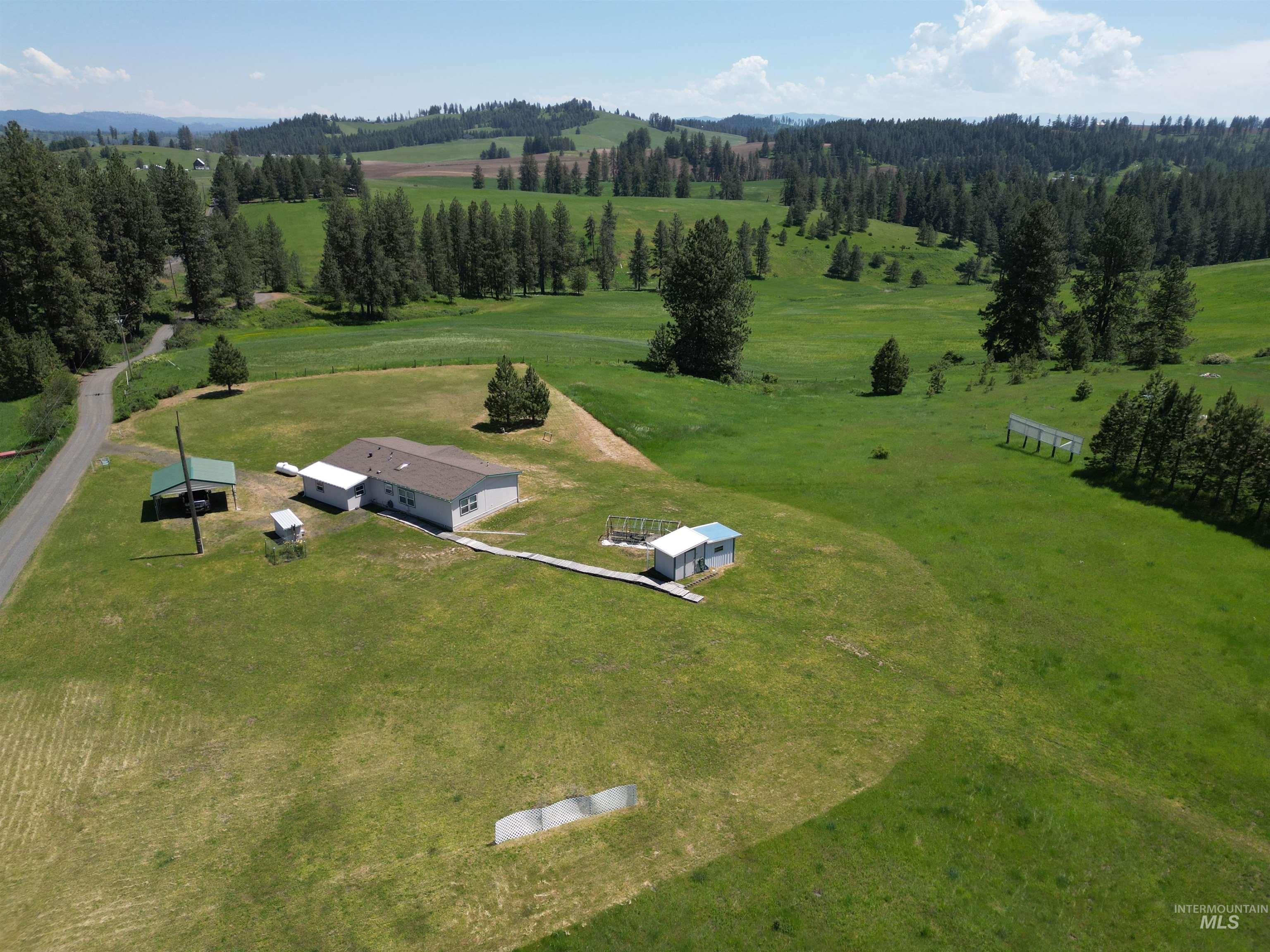 135 Harrisburg Road Kamiah, ID 83536 - Photo 18 of 41 Expansive rural property featuring a single-story residence with a brown shingle roof, a separate carport with a green metal roof, and an additional outbuilding with a light blue metal roof