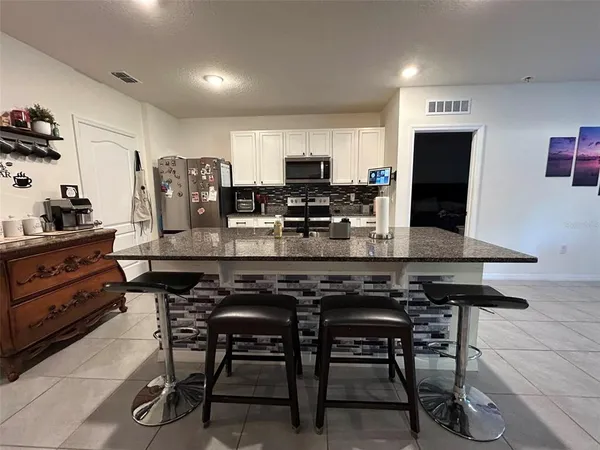 a kitchen with stainless steel appliances kitchen island granite countertop a table chairs sink and cabinets