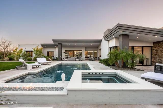 a view of a white house in front of a big yard with plants and large trees