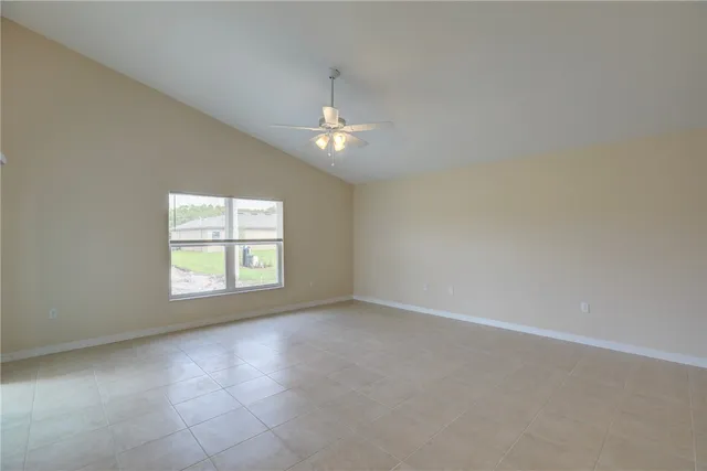 an empty room with chandelier fan and windows