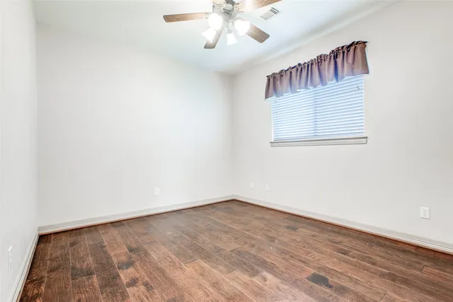 an empty room with wooden floor chandelier fan and windows