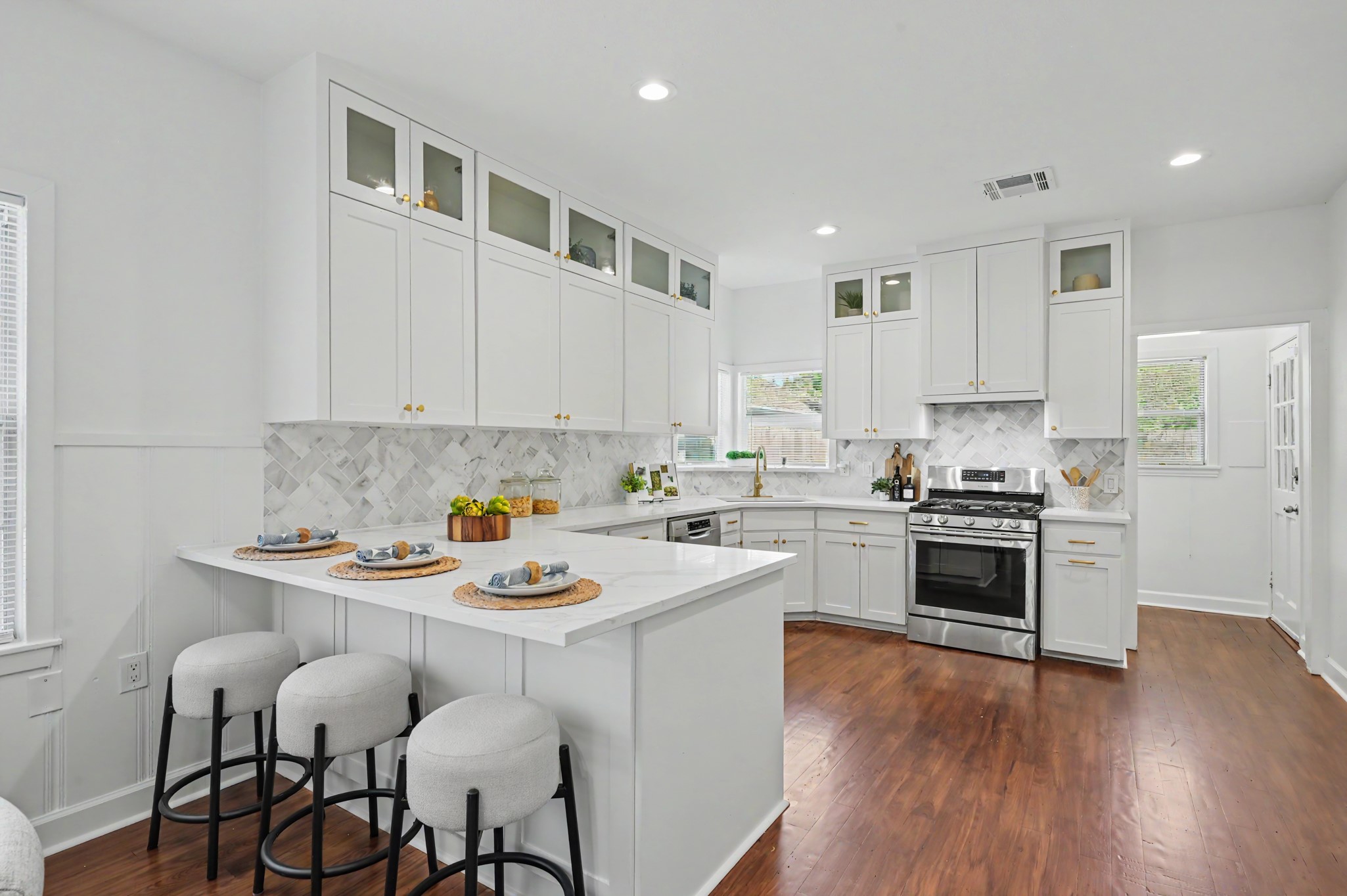 807 Key Street Houston, TX 77009 - Photo 12 of 27 White cabinetry, quartz countertops, stainless steel appliances, brass hardware, and a patterned marble tile backsplash.