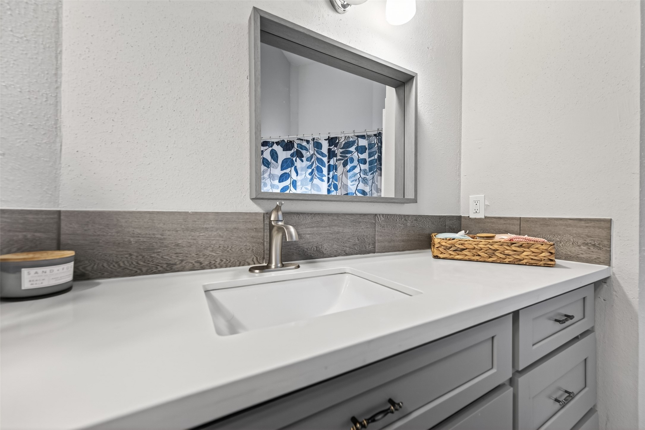 18446 North Willow Bluff Road Katy, TX 77449 - Photo 23 of 33 This bathroom features a sleek, modern vanity with a white countertop and undermount sink. It includes ample storage with several drawers, a stylish faucet, a framed mirror, and a decorative tile backsplash. A hint of color is added by the shower curtain with a blue leaf pattern.