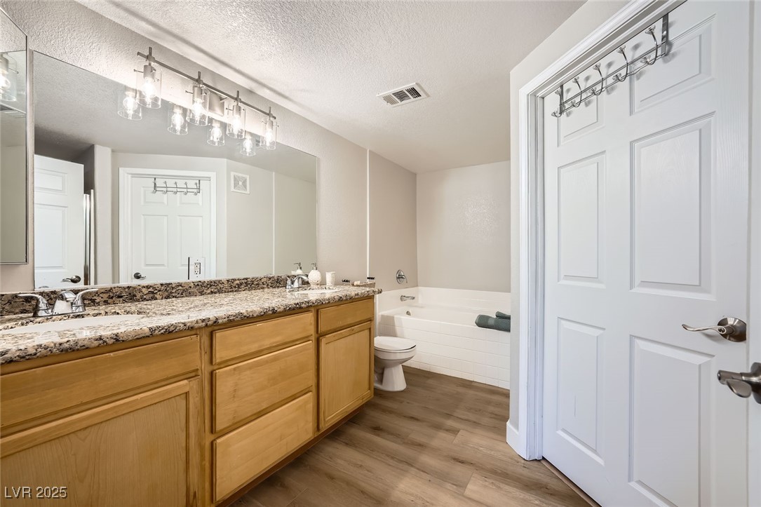 10550 West Alexander Road, Unit 2179 Las Vegas, NV 89129 - Photo 16 of 28 Bathroom with wood finished floors, a sink, a textured ceiling, a bath, and double vanity