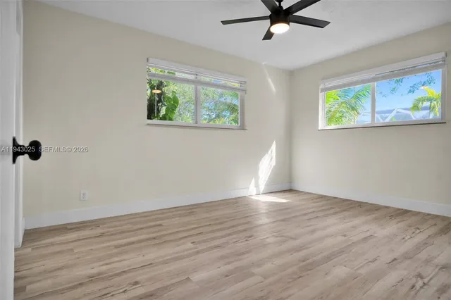 an empty room with wooden floor ceiling fan and windows