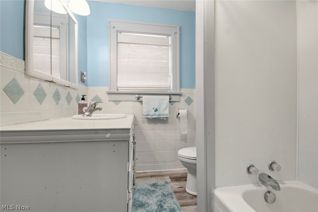 32 Como Street Struthers, OH 44471 - Photo 17 of 22 Full bathroom with a wainscoted wall, vanity, tile walls, a garden tub, and light wood finished floors