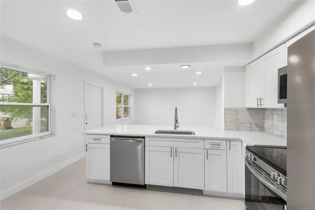 a kitchen with white cabinets appliances a sink and a window