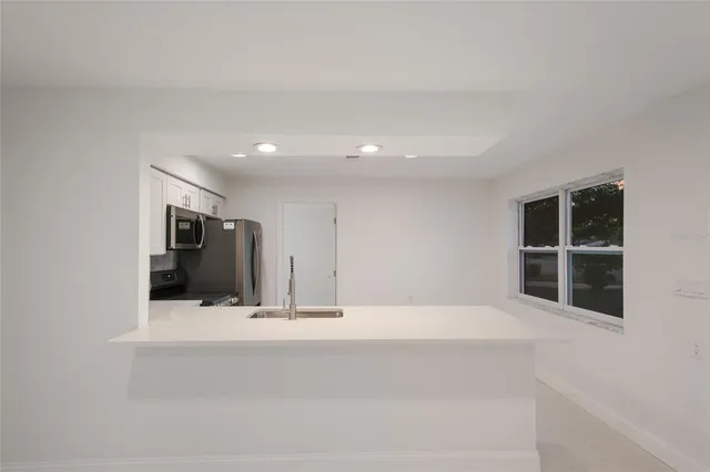 a view of an empty room with kitchen and window