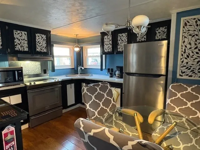 a kitchen with stainless steel appliances granite countertop a refrigerator a sink dishwasher a stove and a dining table with wooden floor