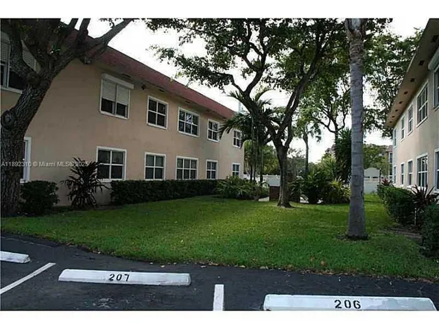 a view of a white house next to a yard with big trees