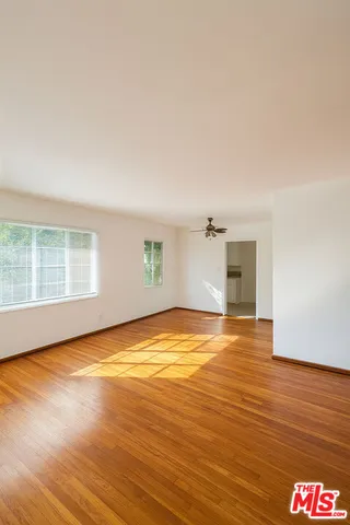 a view of empty room with wooden floor and fan