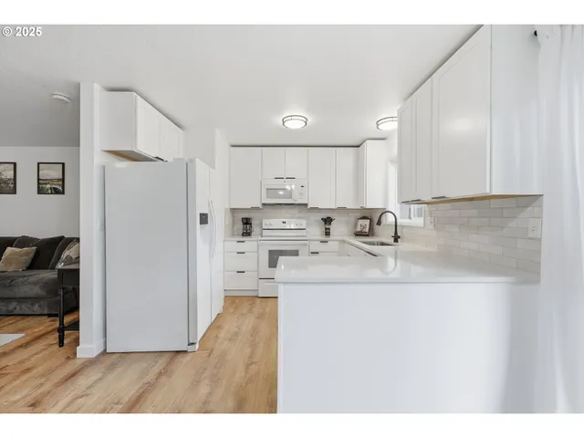 a kitchen with stainless steel appliances granite countertop a refrigerator a sink a stove and white cabinets with wooden floor