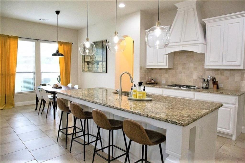 421 Prairie Run Aledo, TX 76008 - Photo 1 of 19 Kitchen featuring backsplash, light stone countertops, white cabinetry, light tile patterned flooring, and a kitchen island with sink