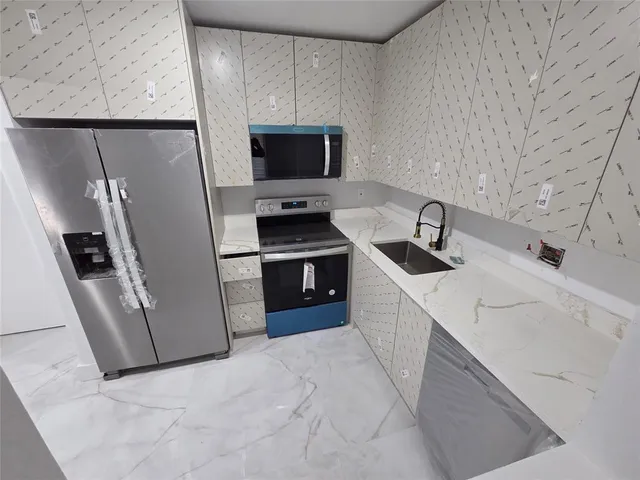 a kitchen with stainless steel appliances a refrigerator a sink a stove and a refrigerator with wooden floor