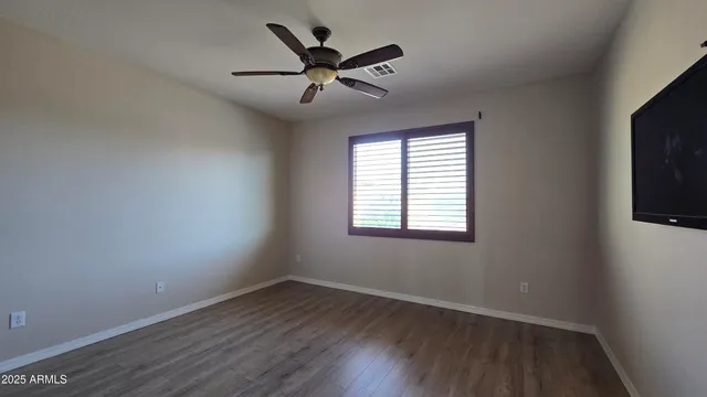 an empty room with wooden floor fan and windows
