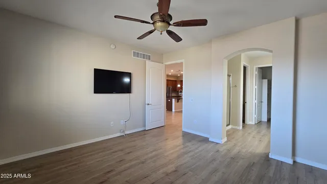 a view of an empty room with wooden floor and a ceiling fan